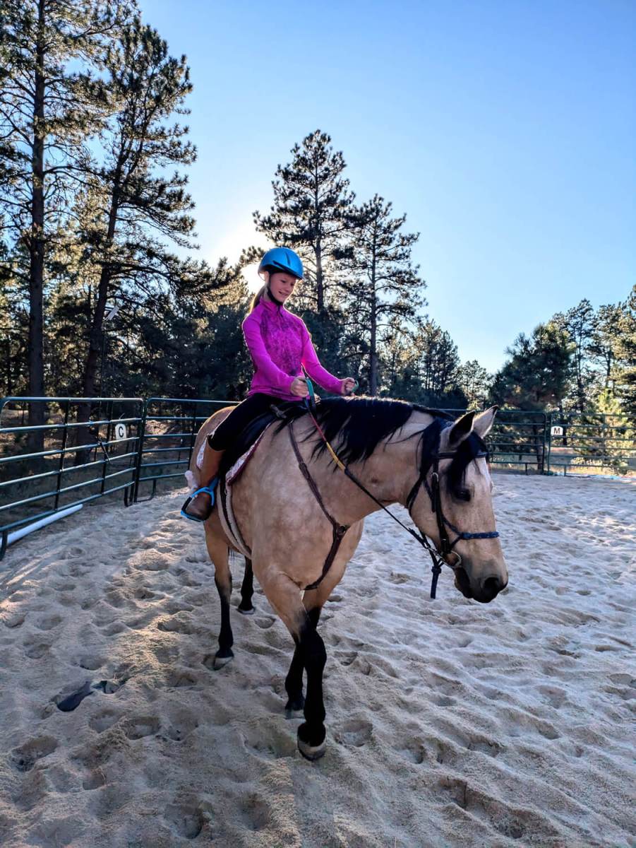 Young rider in magenta jacket on tan horse